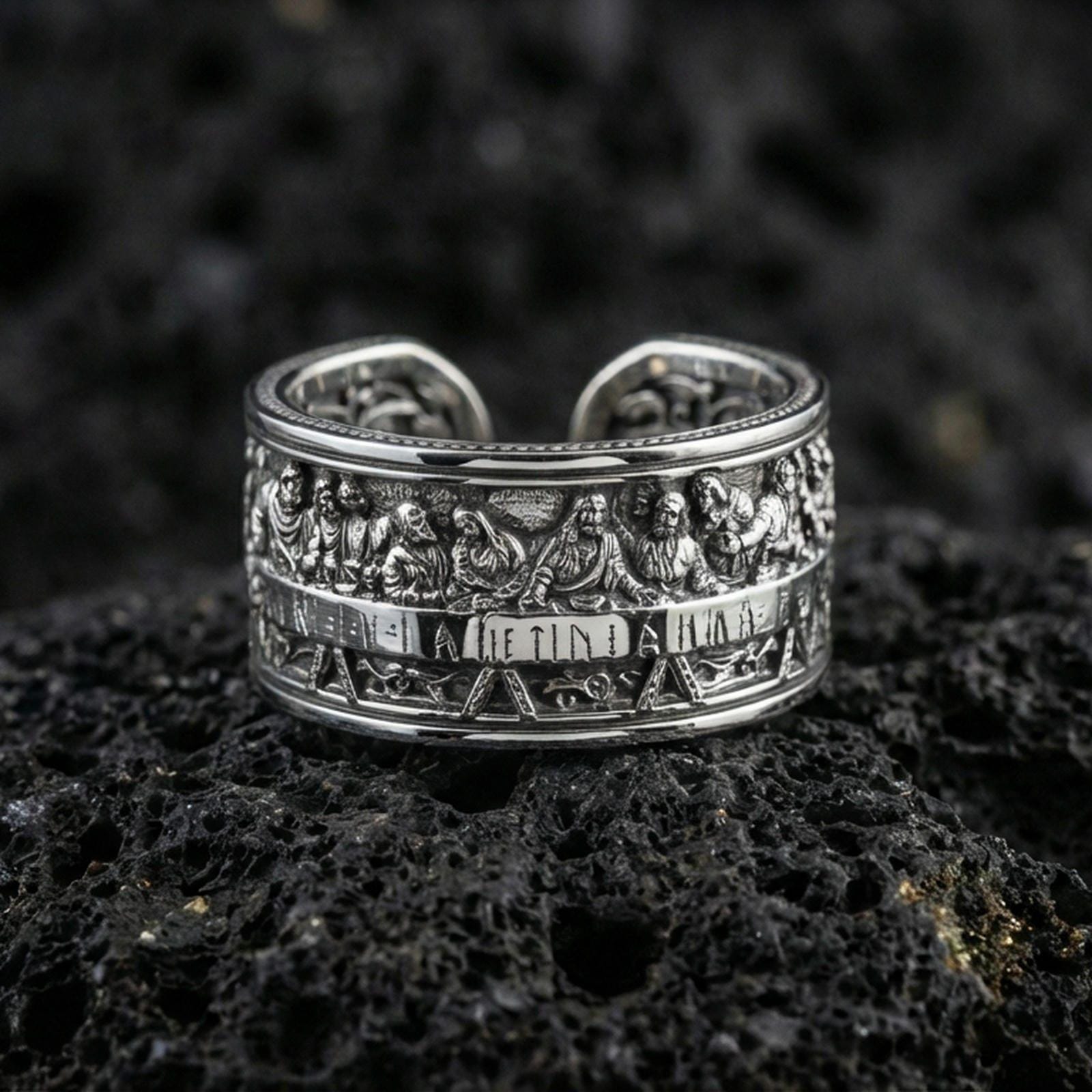 Polished silver Last Supper religious band ring on black volcanic stone, crisp engraved apostle scene relief with smooth comfort edges, centered close-up studio lighting.
