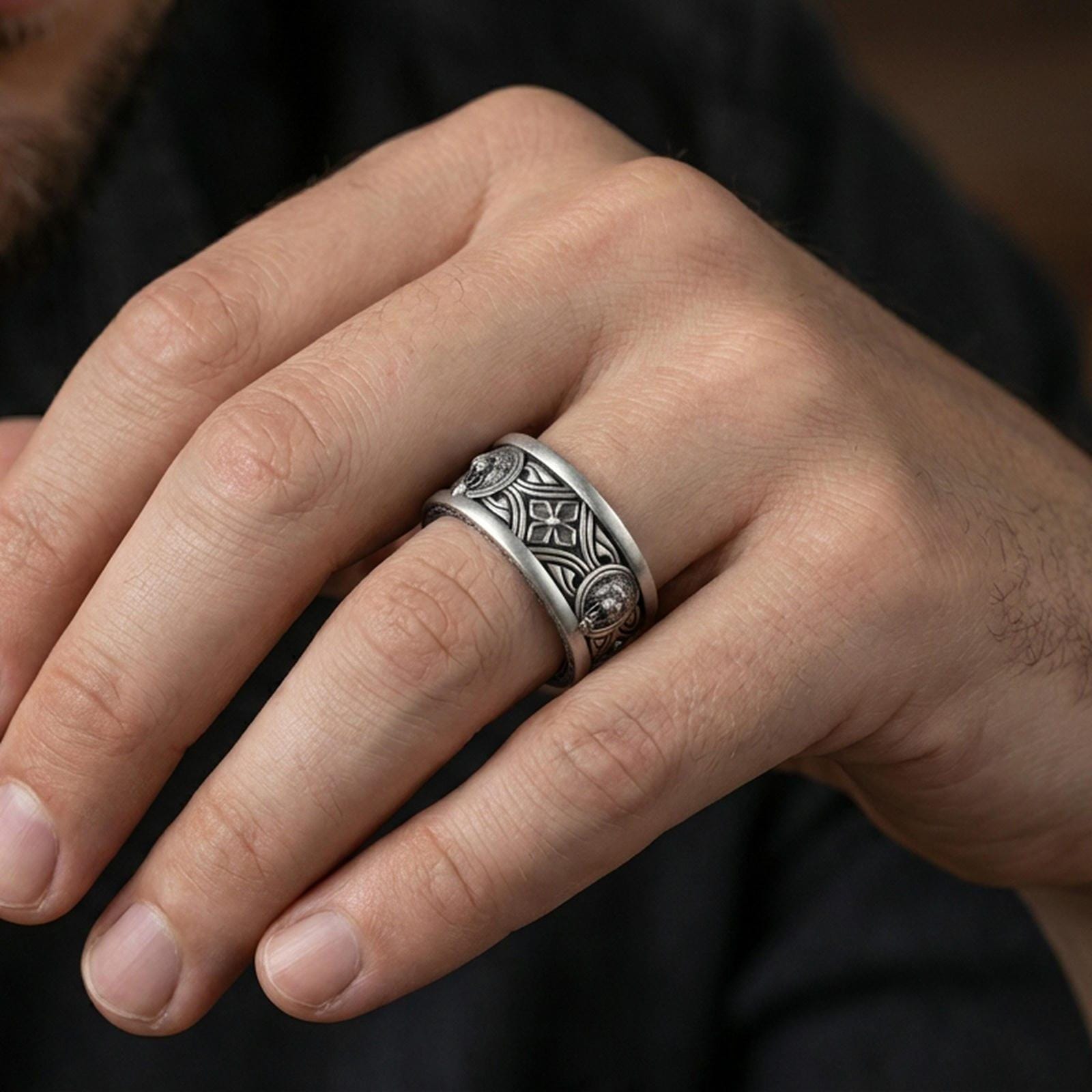 Oxidized sterling silver lion medallion band worn on finger, lion head relief panels and cross motif detail, natural lifestyle hand shot with shallow depth of field.