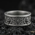 Load image into Gallery viewer, Oxidized sterling silver lion medallion band ring on dark volcanic rock, twin lion head relief panels with gothic cross and scrollwork center, premium macro product shot.
