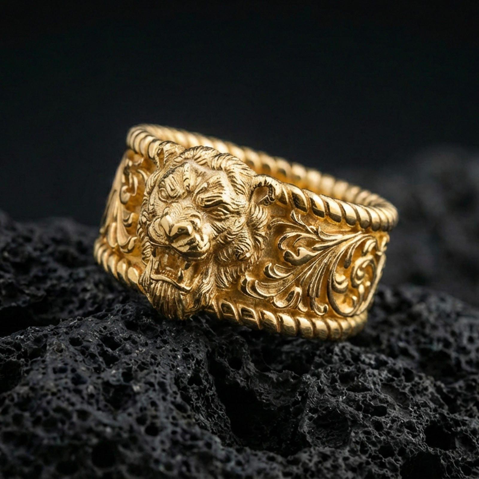 Gold plated lion head signet ring on volcanic rock, detailed roaring lion relief with baroque scrollwork shoulders and rope-edge accents, luxury jewelry product photography.