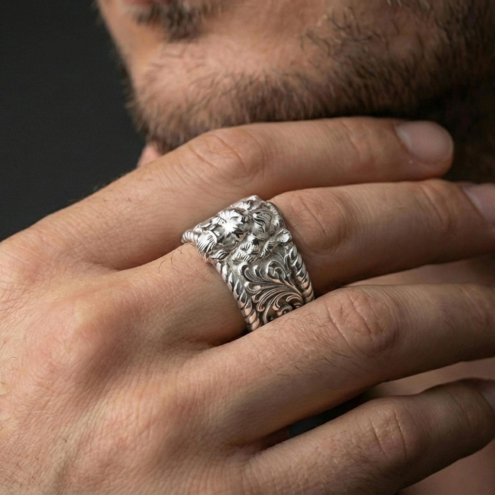 Polished silver lion signet ring on finger, crisp lion head relief with engraved scrollwork sides, refined everyday wear close-up.