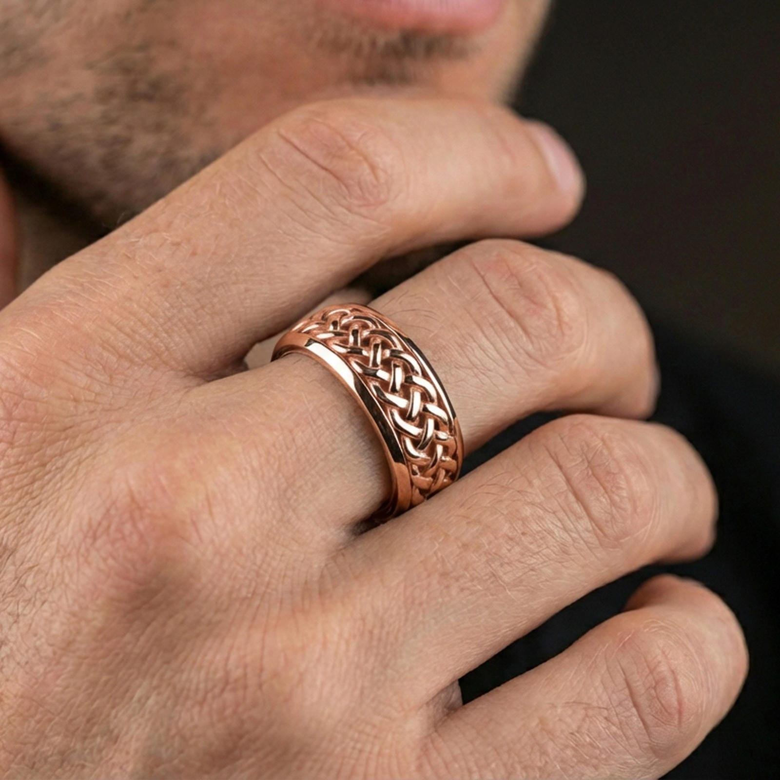 Rose gold plated braided Celtic knot band worn on finger, detailed interwoven texture with elegant contrast, refined lifestyle close-up.