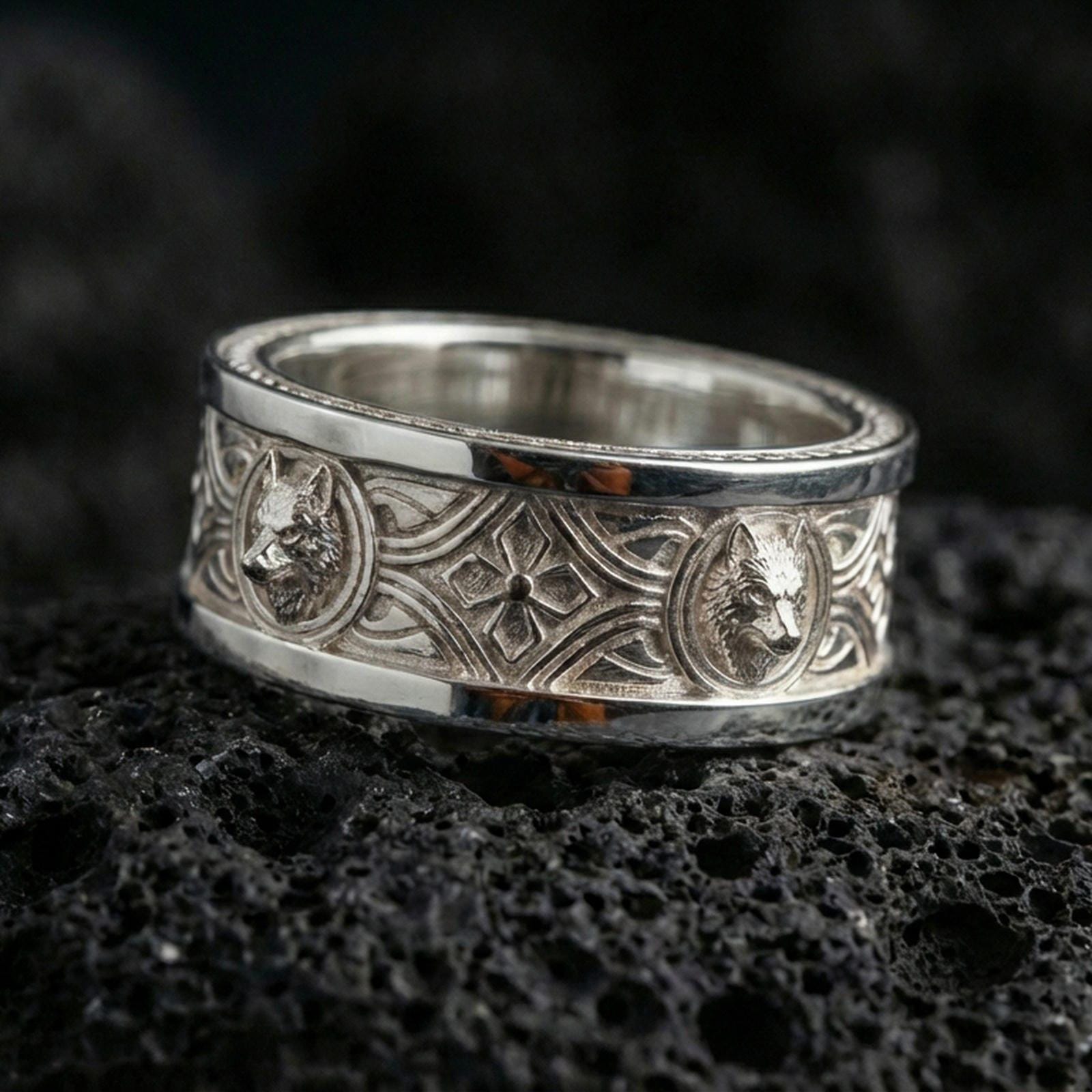 Polished silver wolf Celtic wedding band on dark volcanic stone, clean reflective edges and sharp engraved knotwork, premium close-up.