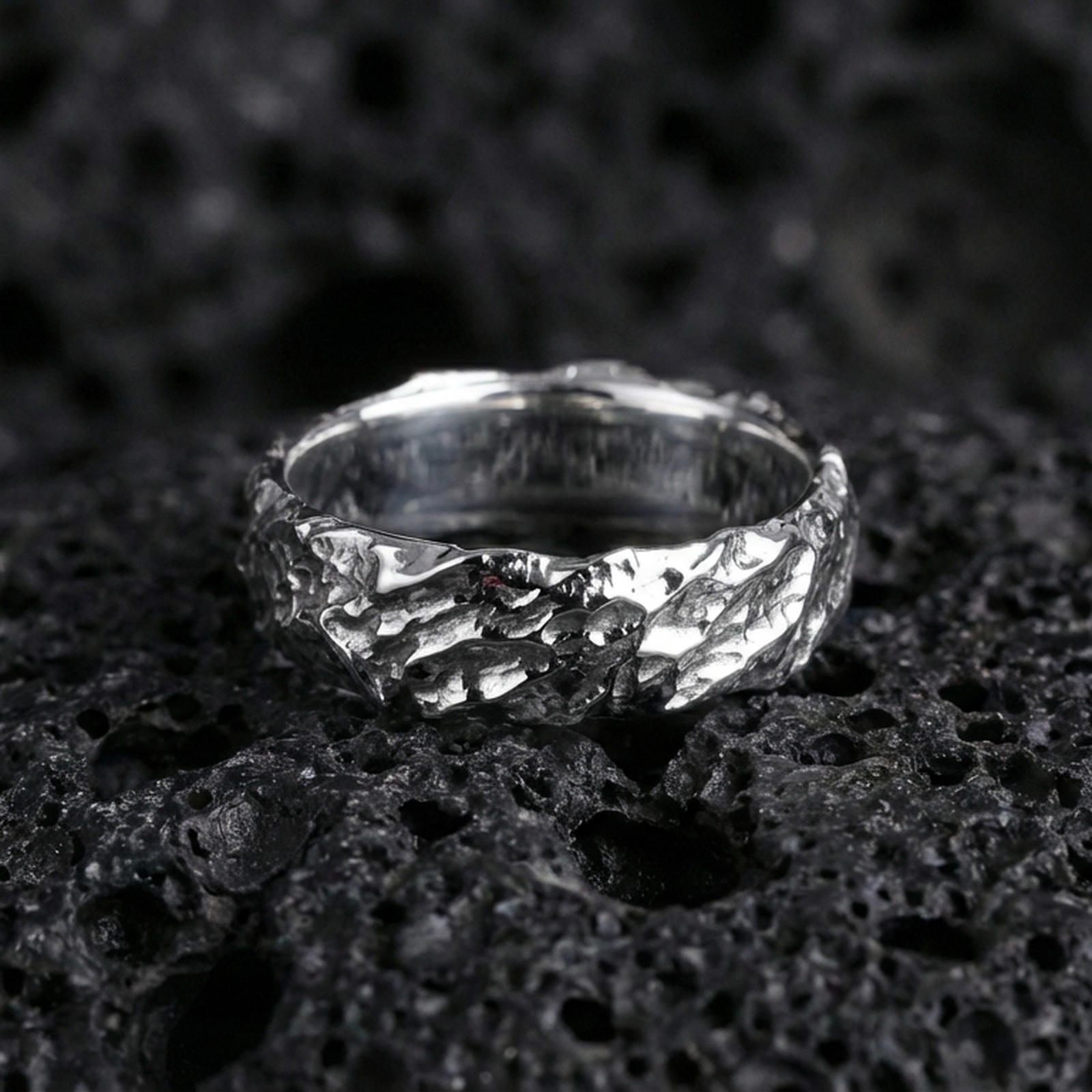 Polished silver hammered organic band on dark volcanic stone, brighter reflective edges with crisp rock-like texture, premium close-up.