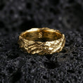 Load image into Gallery viewer, Gold plated rugged hammered ring on volcanic rock, molten lava texture with warm metallic highlights and strong contrast, studio macro.
