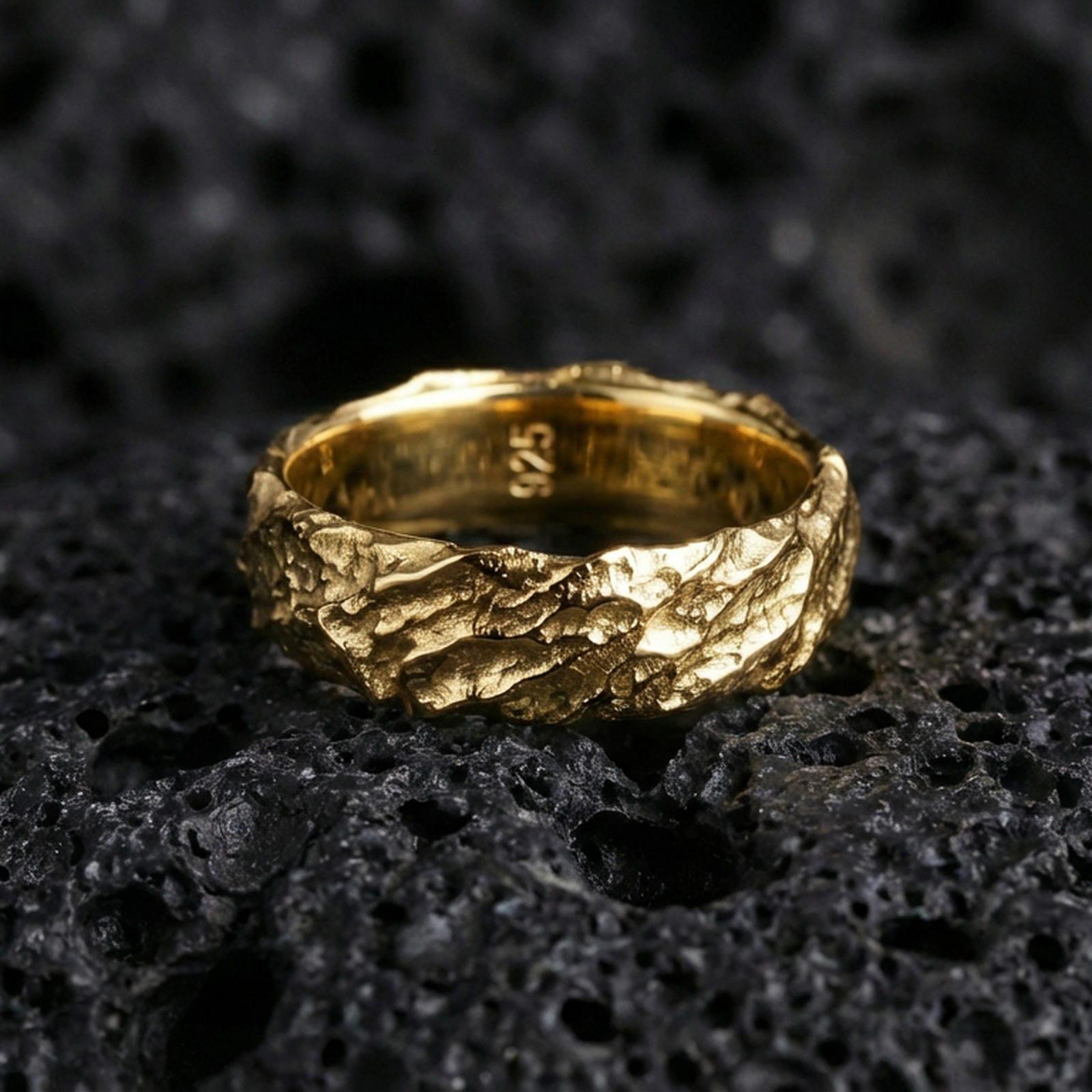 Gold plated rugged hammered ring on volcanic rock, molten lava texture with warm metallic highlights and strong contrast, studio macro.