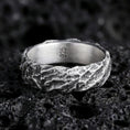 Load image into Gallery viewer, Oxidized sterling silver hammered texture band ring on black volcanic rock, rugged molten-stone surface with deep shadowed crevices, macro product photo.
