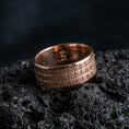 Load image into Gallery viewer, Rose gold plated geometric grid band ring on volcanic rock, soft warm highlights across the repeated square pattern, luxury product shot.
