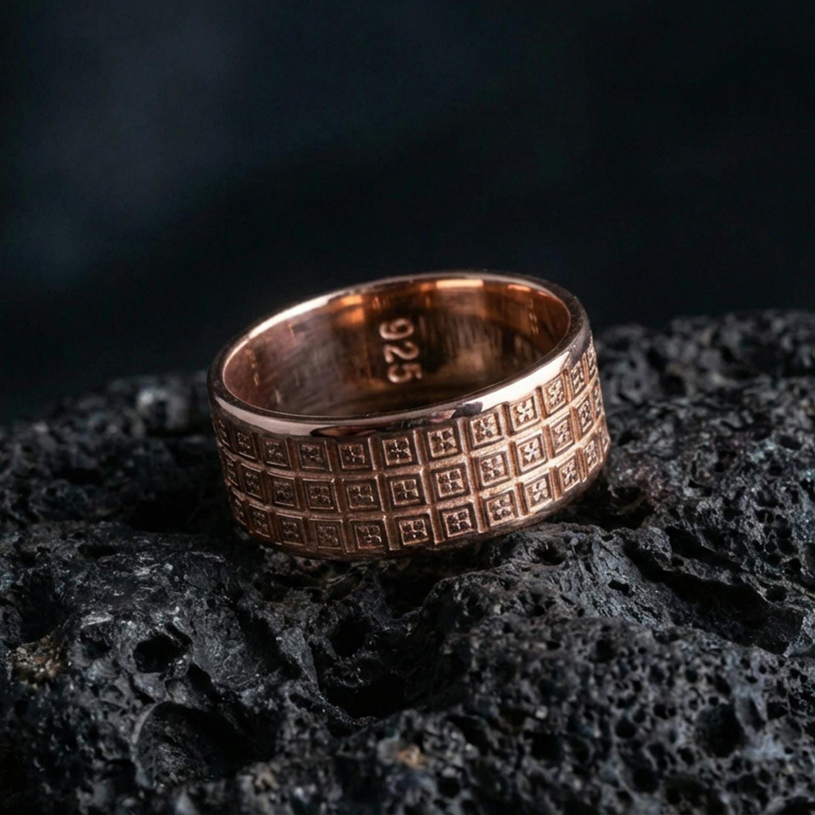 Rose gold plated geometric grid band ring on volcanic rock, soft warm highlights across the repeated square pattern, luxury product shot.