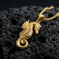 Load image into Gallery viewer, Gold plated seahorse pendant with sculpted marine texture, curled tail design, and elegant underwater silhouette showcased on black volcanic rock in a refined macro jewelry image
