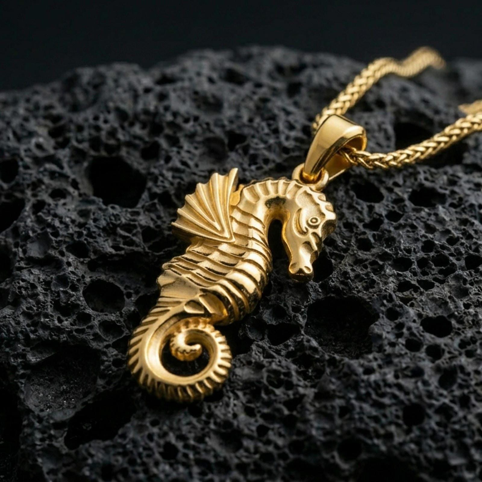 Gold plated seahorse pendant with sculpted marine texture, curled tail design, and elegant underwater silhouette showcased on black volcanic rock in a refined macro jewelry image