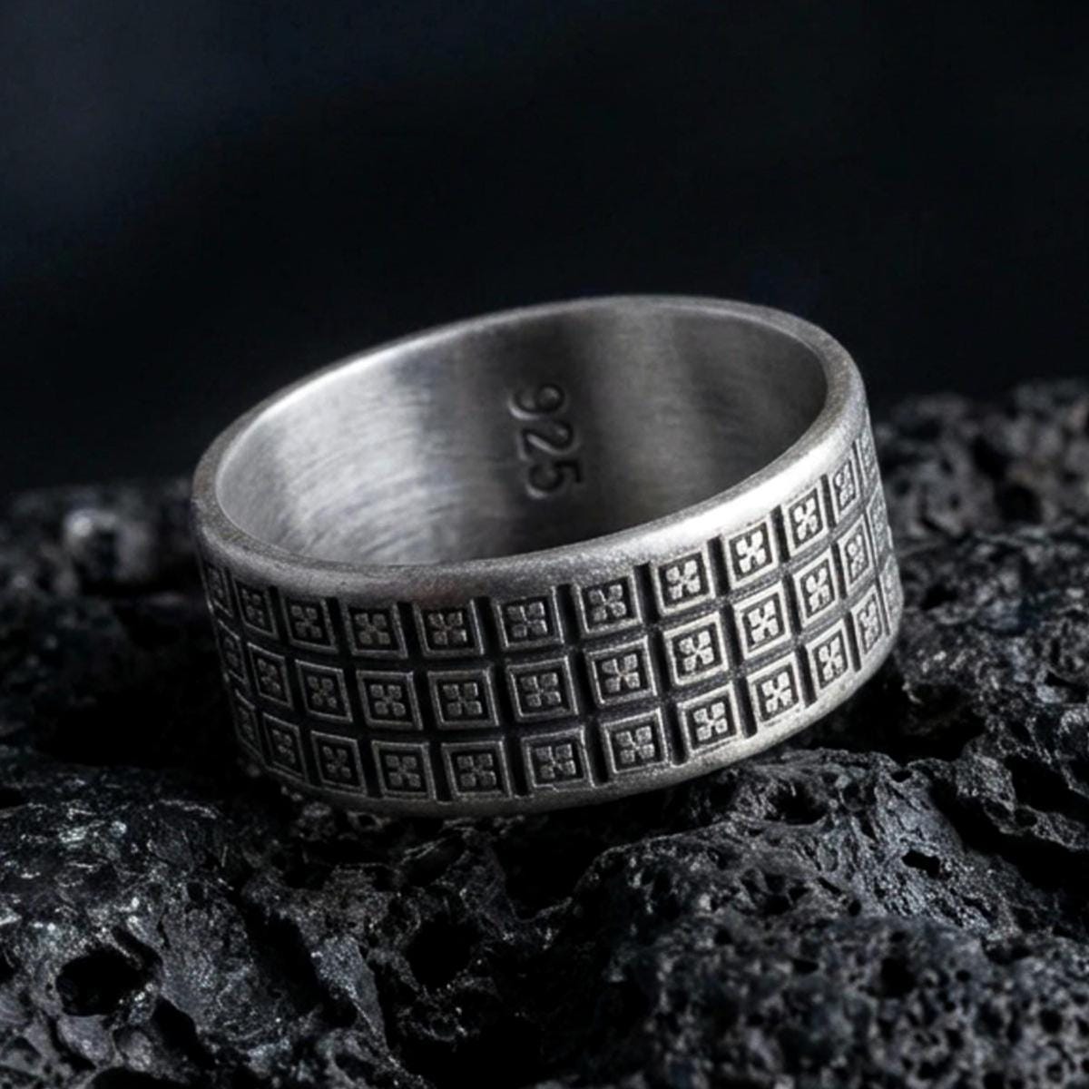 Oxidized sterling silver geometric square-grid ring on black volcanic stone, darkened recesses emphasizing the tiny cross-in-square texture, macro product photo.