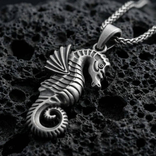 Oxidized seahorse pendant with sculpted marine details, curled tail, and textured nautical silhouette displayed on dark volcanic rock in a close-up luxury jewelry composition