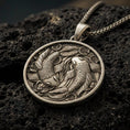 Load image into Gallery viewer, Bronze koi fish pendant with yin yang-inspired twin fish design, flowing water details, and round medallion silhouette displayed on dark volcanic rock in a close-up luxury jewelry composition
