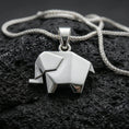 Load image into Gallery viewer, Polished silver elephant necklace with angular origami-inspired structure, clean faceted surfaces, and modern animal design placed on textured volcanic rock in a premium studio product shot
