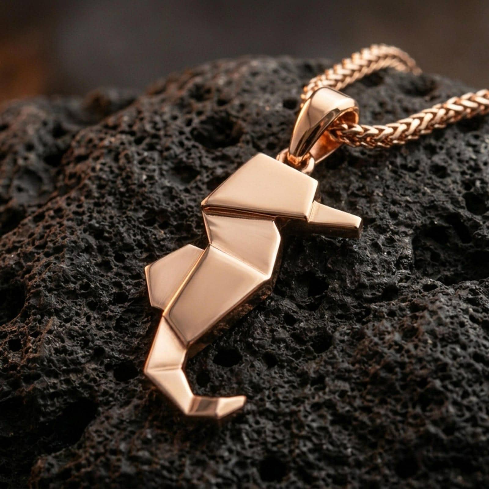 Rose gold plated geometric seahorse necklace with clean angular folds, elegant marine shape, and contemporary minimalist styling resting on volcanic rock in an elegant close-up product presentation