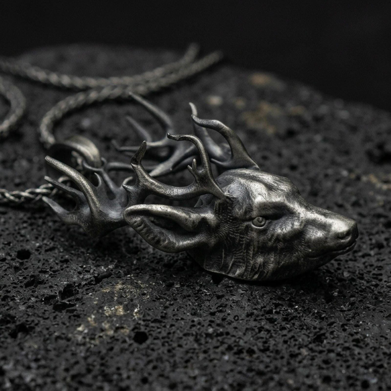 Oxidized stag pendant with detailed deer head, branching antlers, and realistic wildlife silhouette displayed on dark volcanic rock in a close-up luxury jewelry composition