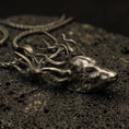 Load image into Gallery viewer, Bronze stag pendant with detailed deer head, branching antlers, and realistic wildlife silhouette displayed on dark volcanic rock in a close-up luxury jewelry composition

