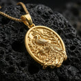 Load image into Gallery viewer, Gold plated peacock pendant with intricate feather pattern, floral vine motifs, and refined oval bird medallion design showcased on black volcanic rock in a refined macro jewelry image
