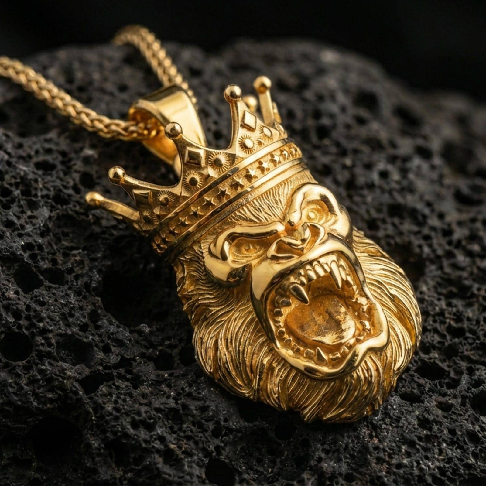 Gold plated gorilla king pendant with regal crown detail, roaring ape relief, and powerful statement silhouette showcased on black volcanic rock in a refined macro jewelry image