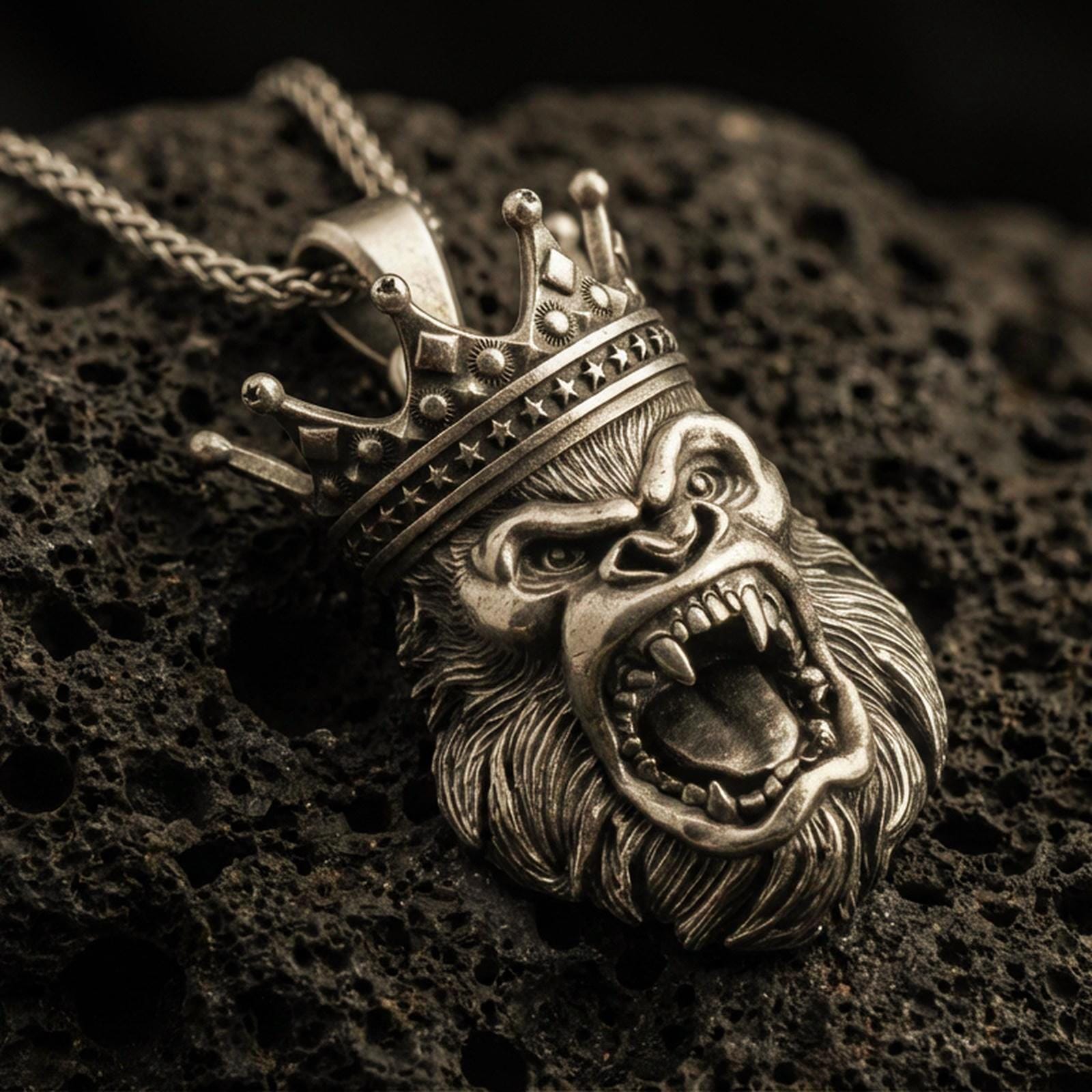 Bronze gorilla king pendant with roaring ape face, detailed crown, and bold animal head silhouette displayed on dark volcanic rock in a close-up luxury jewelry composition