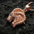 Load image into Gallery viewer, Rose gold plated ram necklace with detailed goat head relief, curved horn silhouette, and elegant astrology-inspired design resting on volcanic rock in an elegant close-up product presentation
