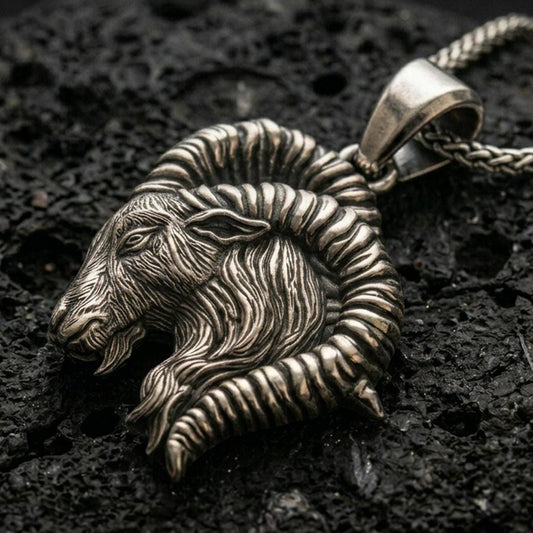 Oxidized Aries ram pendant with detailed horn curve, textured goat head relief, and zodiac-inspired animal silhouette displayed on dark volcanic rock in a close-up luxury jewelry composition