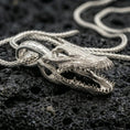 Load image into Gallery viewer, Polished silver gator skull necklace with sculpted reptile head, sharp teeth detailing, and realistic skull structure placed on textured volcanic rock in a premium studio product shot
