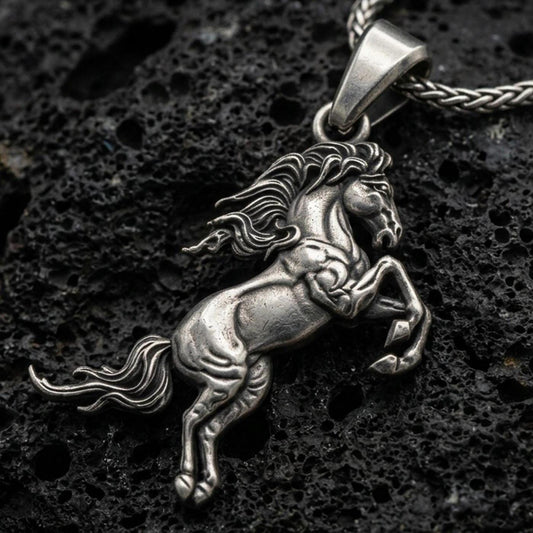 Oxidized horse pendant with rearing equine silhouette, flowing mane, and detailed muscular form displayed on dark volcanic rock in a close-up luxury jewelry composition