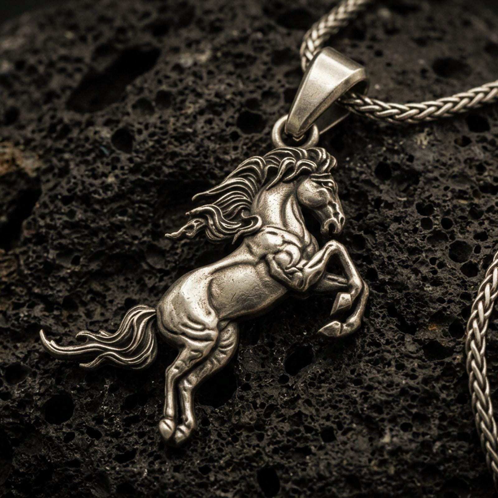 Bronze horse pendant with rearing equine silhouette, flowing mane, and detailed muscular form displayed on dark volcanic rock in a close-up luxury jewelry composition