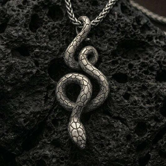 Oxidized snake pendant with coiled serpent silhouette and detailed scale texture displayed on dark volcanic rock in a close-up luxury jewelry composition