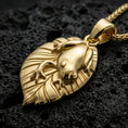 Load image into Gallery viewer, Gold plated frog pendant with detailed amphibian body, leaf motif foundation, and elegant nature-inspired design showcased on black volcanic rock in a refined macro jewelry image
