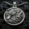 Load image into Gallery viewer, Oxidized twin wolf pendant with flowing fur detail, howling and resting wolf relief, and round medallion silhouette displayed on dark volcanic rock in a close-up luxury jewelry composition
