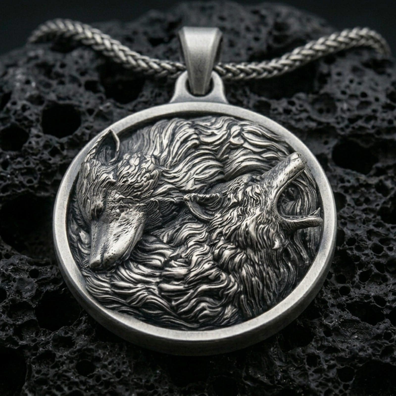 Oxidized twin wolf pendant with flowing fur detail, howling and resting wolf relief, and round medallion silhouette displayed on dark volcanic rock in a close-up luxury jewelry composition