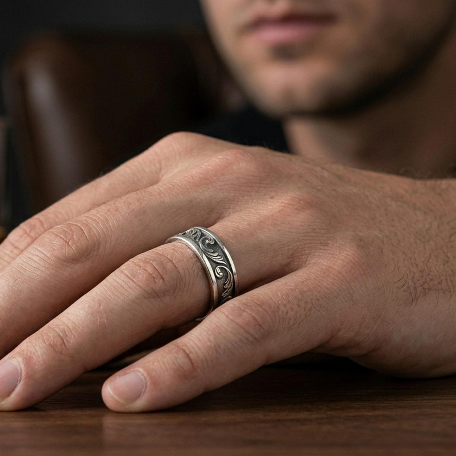 Oxidized sterling silver engraved floral band worn on finger, darkened relief showing the vine-scroll pattern with a subtle vintage look.