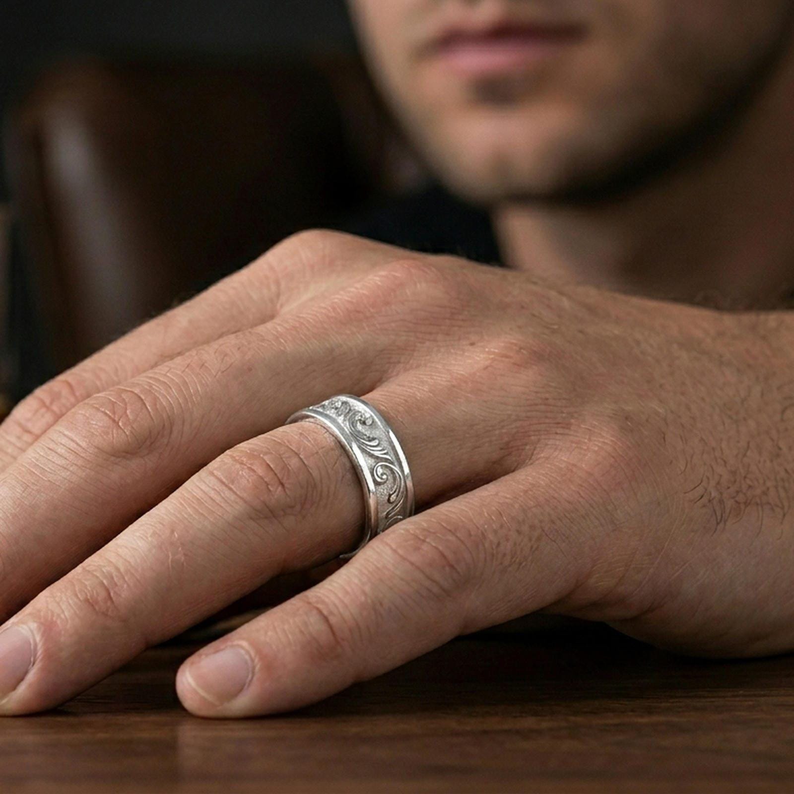 Polished silver minimalist floral wedding band worn on finger, sleek comfort fit with sharp engraved scroll details in natural light.