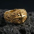 Load image into Gallery viewer, Gold plated North Star compass ring on black volcanic stone, warm reflective finish emphasizing the hand-carved star facets and ornamental scrolls.
