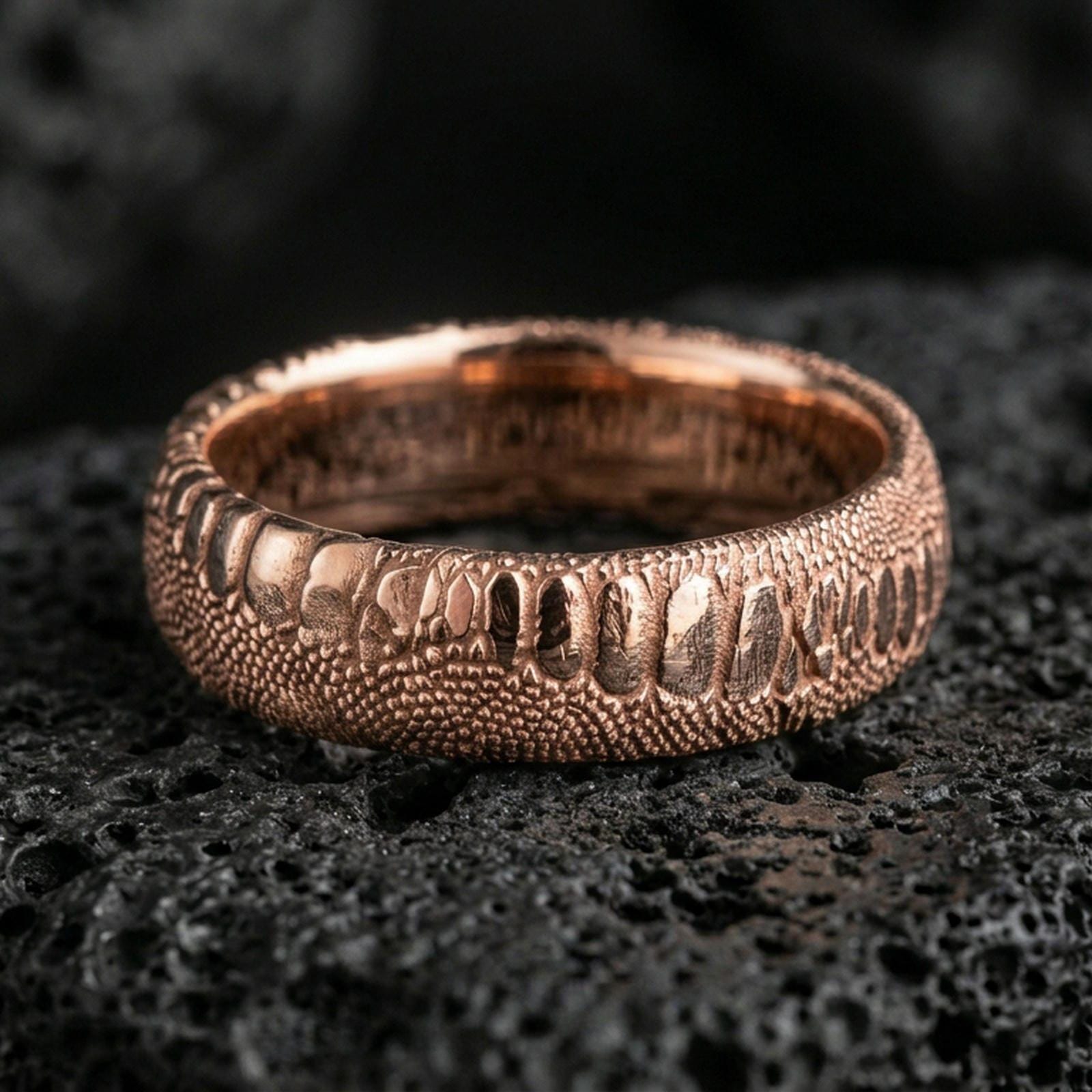 Rose gold plated snake scale band ring on volcanic rock, soft warm tone highlighting the reptile skin pattern and sculpted edges.
