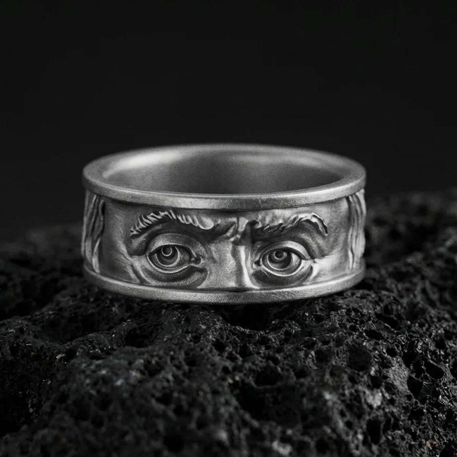 Oxidized sterling silver Benjamin Franklin eyes band ring on black volcanic stone, deepened shadows emphasizing the facial relief and intense gaze.