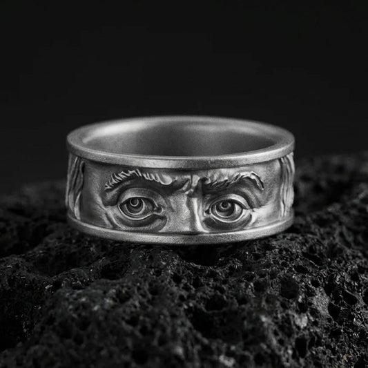 Oxidized sterling silver Benjamin Franklin eyes band ring on black volcanic stone, deepened shadows emphasizing the facial relief and intense gaze.