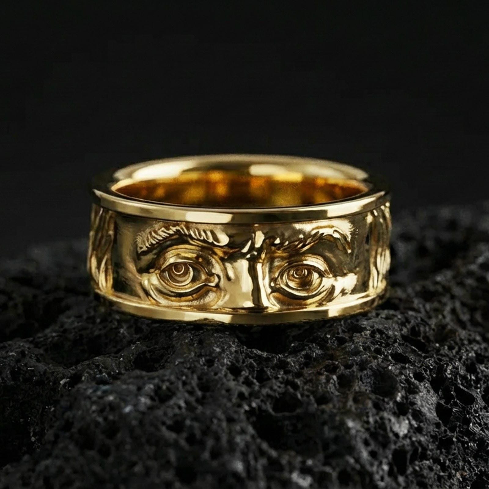 Gold plated Benjamin Franklin eyes ring on black volcanic stone, warm luminous tone highlighting the sculpted brow and engraved depth.