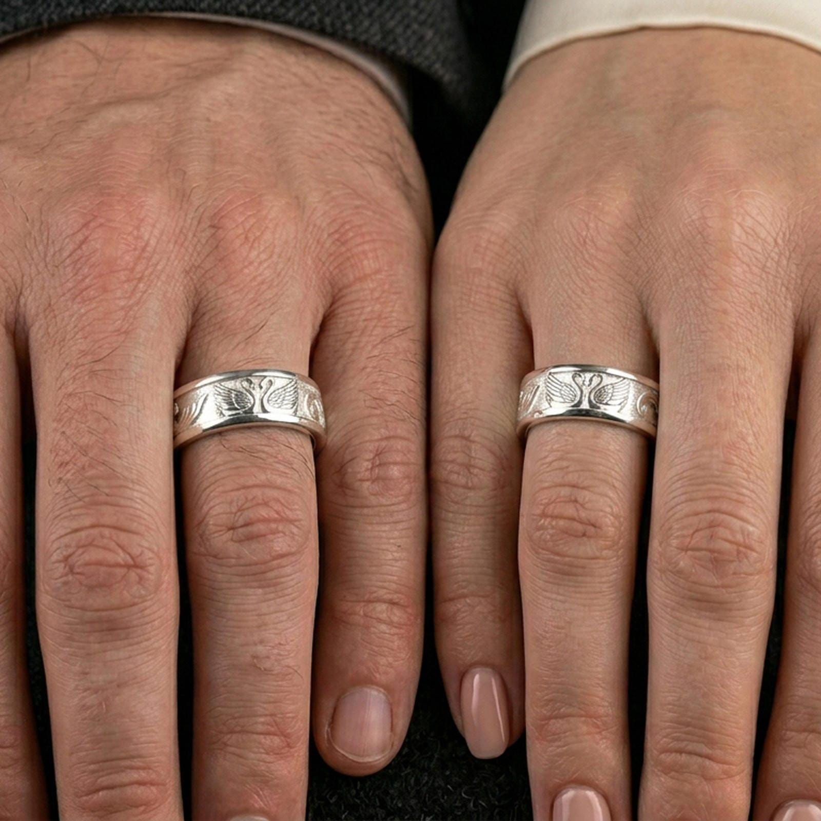 Polished silver swan band ring on a finger, clean shine along the rim with detailed swan wings across the center.