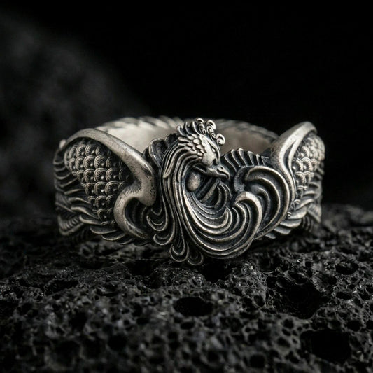 Sterling silver rooster ring photographed on volcanic rock with oxidized contrast emphasizing the carved feathers and bold crest detail.