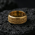 Load image into Gallery viewer, Fleur de lis patterned ring displayed on volcanic rock with a gold plated finish, highlighting the raised symbols and textured band.
