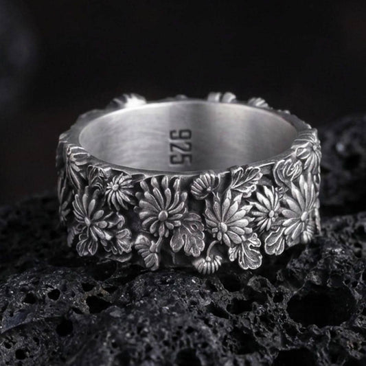 Sterling silver floral band ring photographed on volcanic rock with oxidized contrast highlighting the raised daisy and leaf relief.