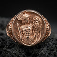 Load image into Gallery viewer, A rose gold plated Medusa head signet ring on volcanic rock, bold oval face with mythological warrior symbolism.
