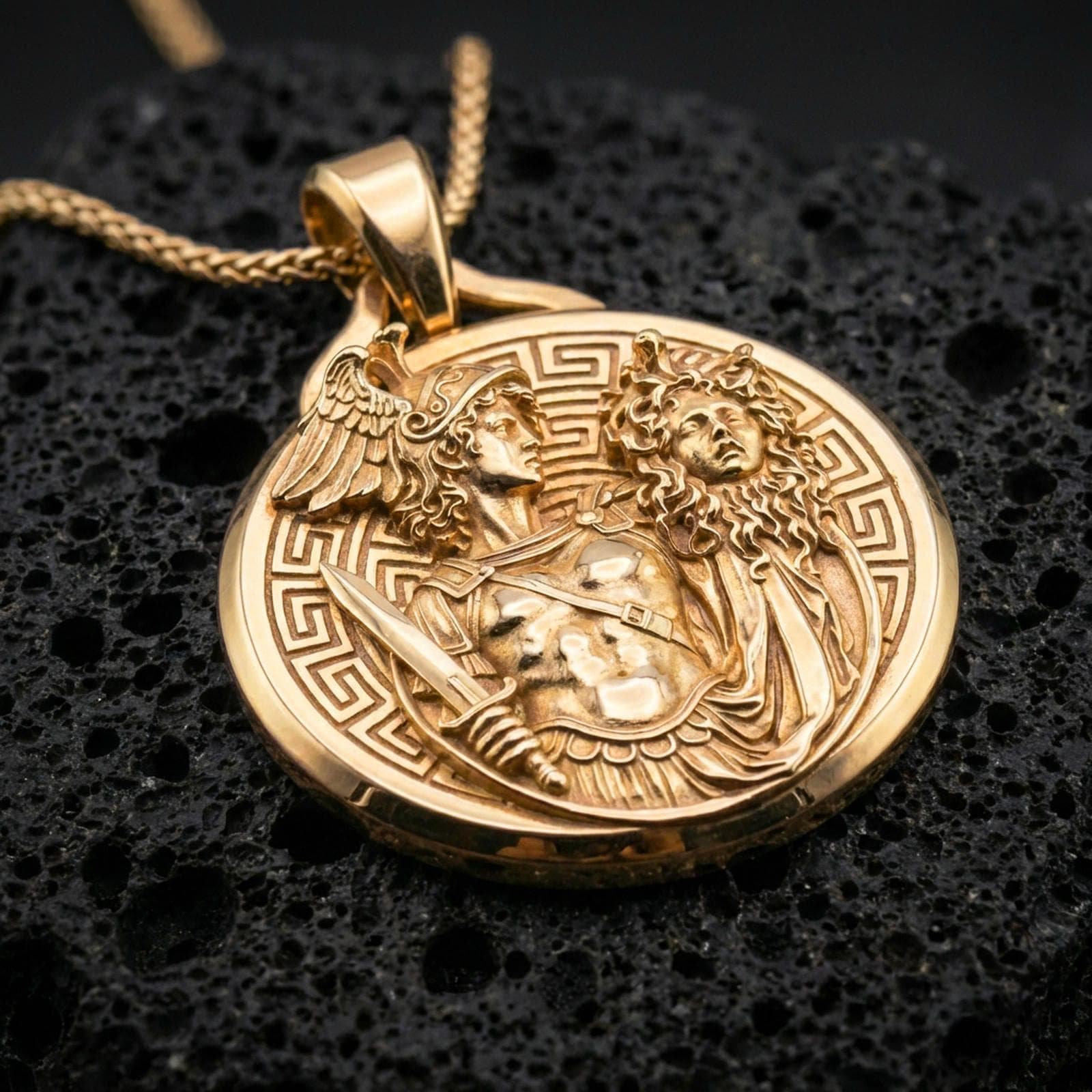 A gold plated Perseus and Medusa pendant necklace on black volcanic stone, coin medallion relief with Greek key frame.