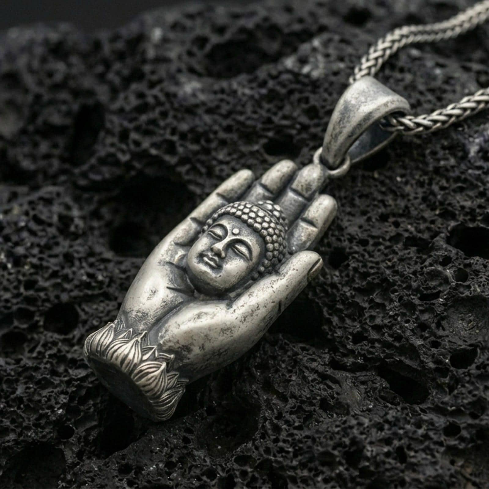 Buddha in protective hand pendant on black volcanic stone with deep oxidized contrast and vintage patina detail.