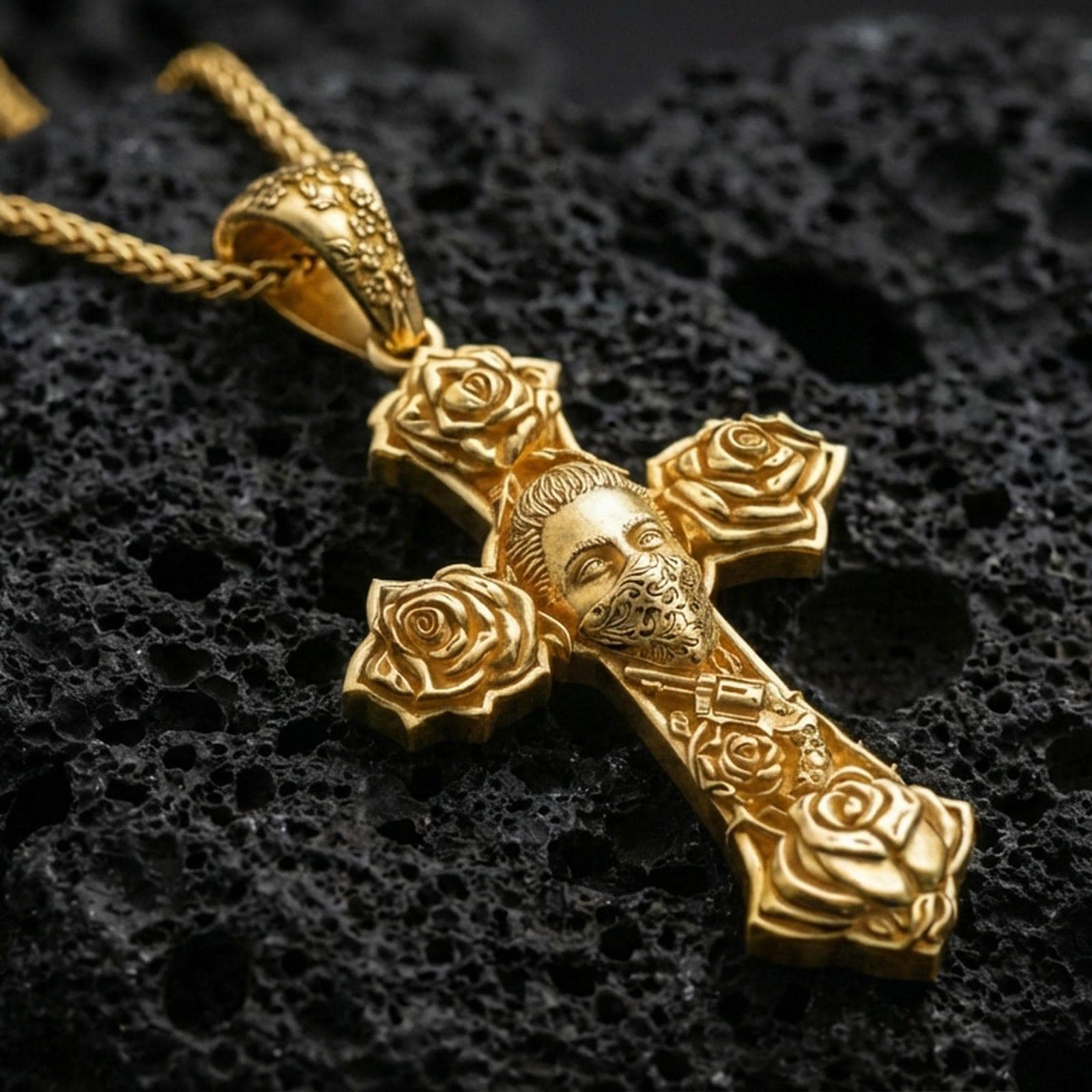 Gold plated cross pendant with Chicano inspired rose accents and detailed masked figure resting on black volcanic rock in a dramatic macro product shot