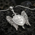 Load image into Gallery viewer, Polished silver spiritual protection pendant with winged shield design and Quis Ut Deus text placed on textured volcanic rock in a premium studio composition
